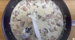Creamy mushroom sauce cooking in a pan, rich and delicious with a spoon stirring ricotta cheese. Great for pasta dishes.